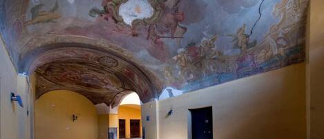 An interior with a high ceiling, ornate frescoes, and a central archway leading to another room.