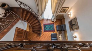 A spiral staircase with ornate metal railings leading to a room with a wooden floor, a patterned rug, and two black leather chairs.