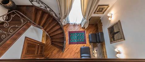 A spiral staircase with ornate metal railings leading to a room with a wooden floor, a patterned rug, and two black leather chairs.
