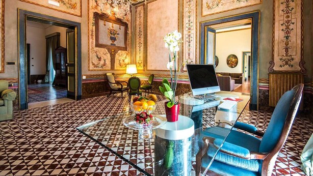 A luxurious room with a patterned floor, a laptop on a glass table, and a blue chair.