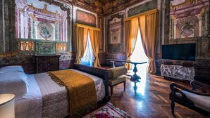 A luxurious bedroom with a large bed, a television, and ornate wall decorations.