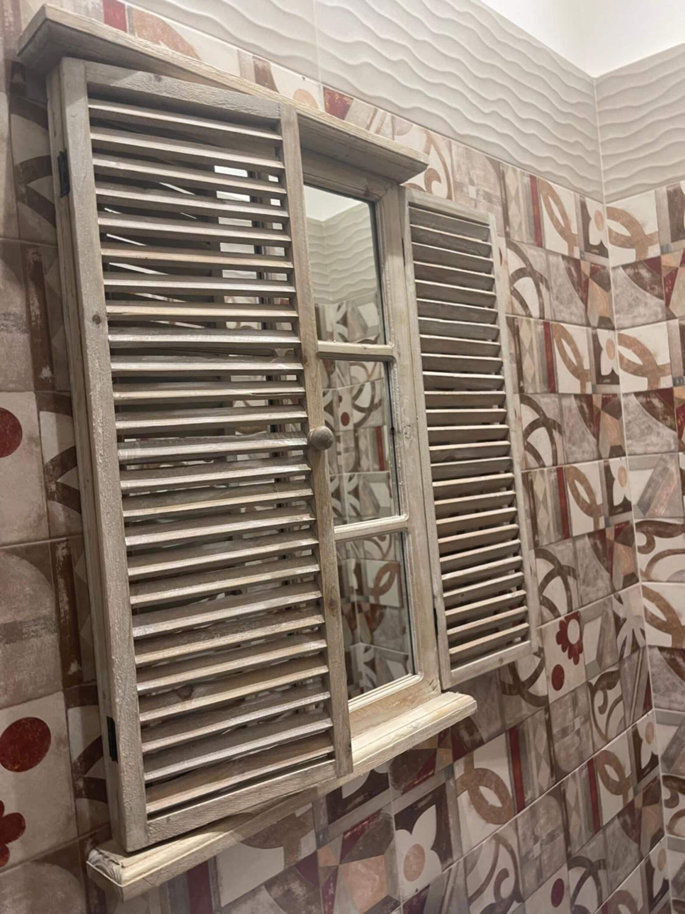 Un baño con baldosas estampadas y contraventanas de madera.