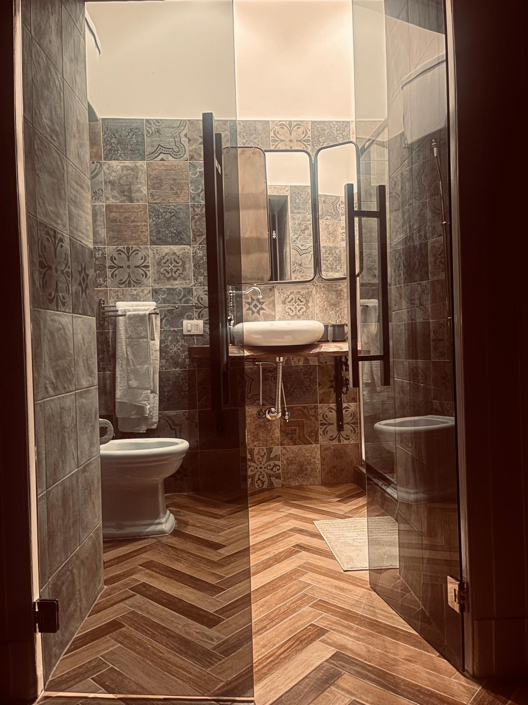 Een badkamer met een visgraat houten vloer, een wit toilet, een wastafel met spiegel en een douchegedeelte.