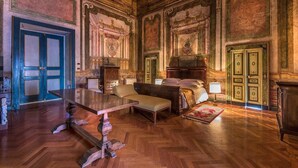 A room with a large wooden desk, a bed with a headboard, and a fireplace.