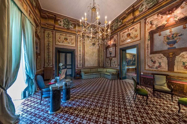 Una habitación con piso a cuadros, un candelabro, un sofá y un escritorio con una computadora.