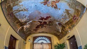 A room with a large, ornate ceiling fresco, a wooden door, and a window with a decorative grille.