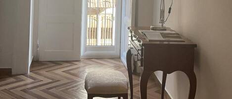 A hallway with a wooden herringbone floor, a white door, a small table with a lamp, and a wall-mounted mirror.
