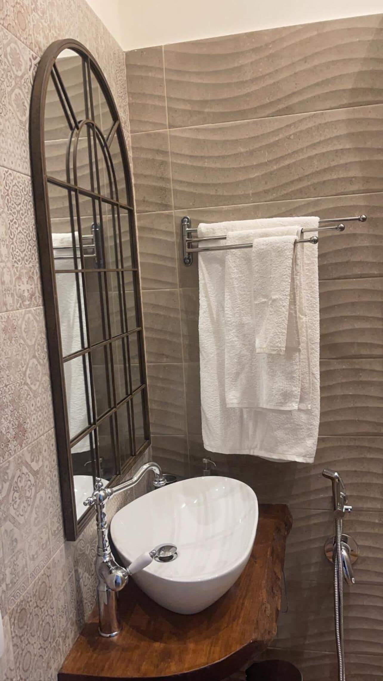 A bathroom with a white sink, a mirror with a metal frame, a towel rack with two towels, and a shower area.