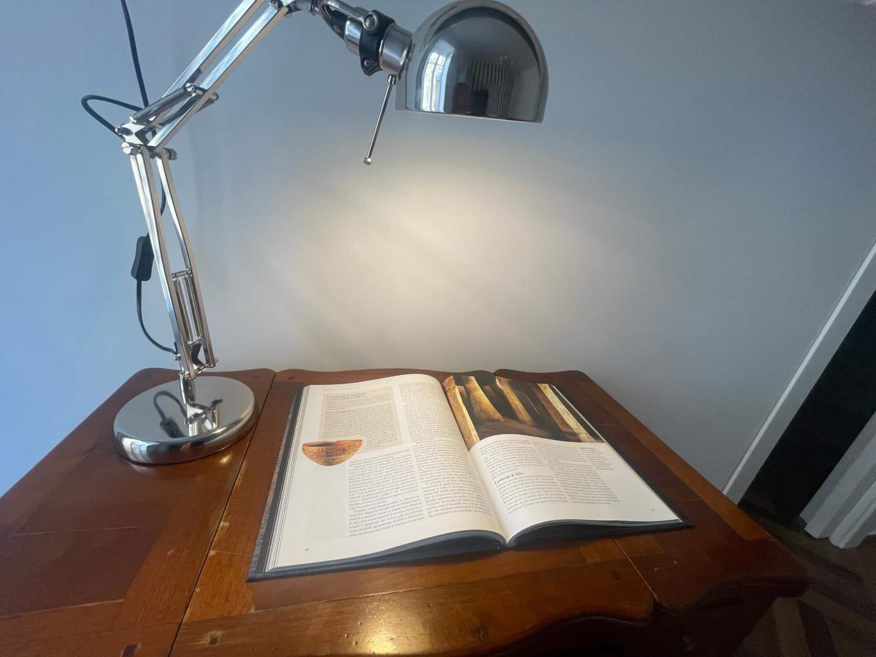 A wooden desk with an open book and a desk lamp.