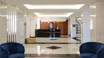 A modern lobby with a reception desk, marble flooring, and two blue armchairs.