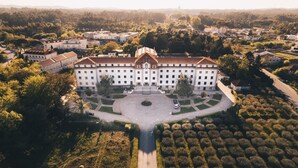 An aerial view of a large, multi-story building with a symmetrical facade, surrounded by a well-maintained garden and a road leading to it. - SDivine Fátima Hotel (Ourem)