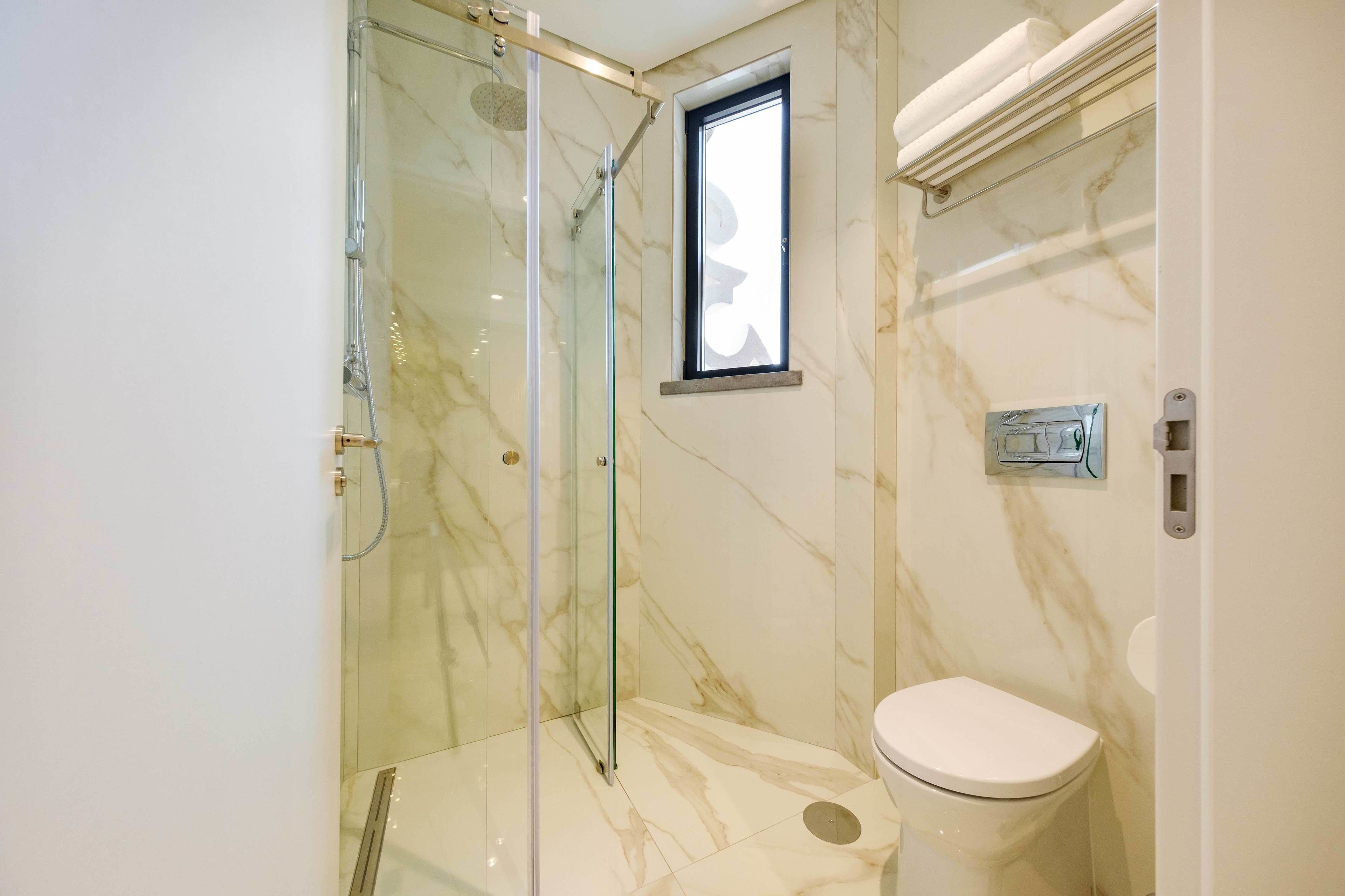 Un baño moderno con cabina de ducha de vidrio, inodoro y pared de mármol.