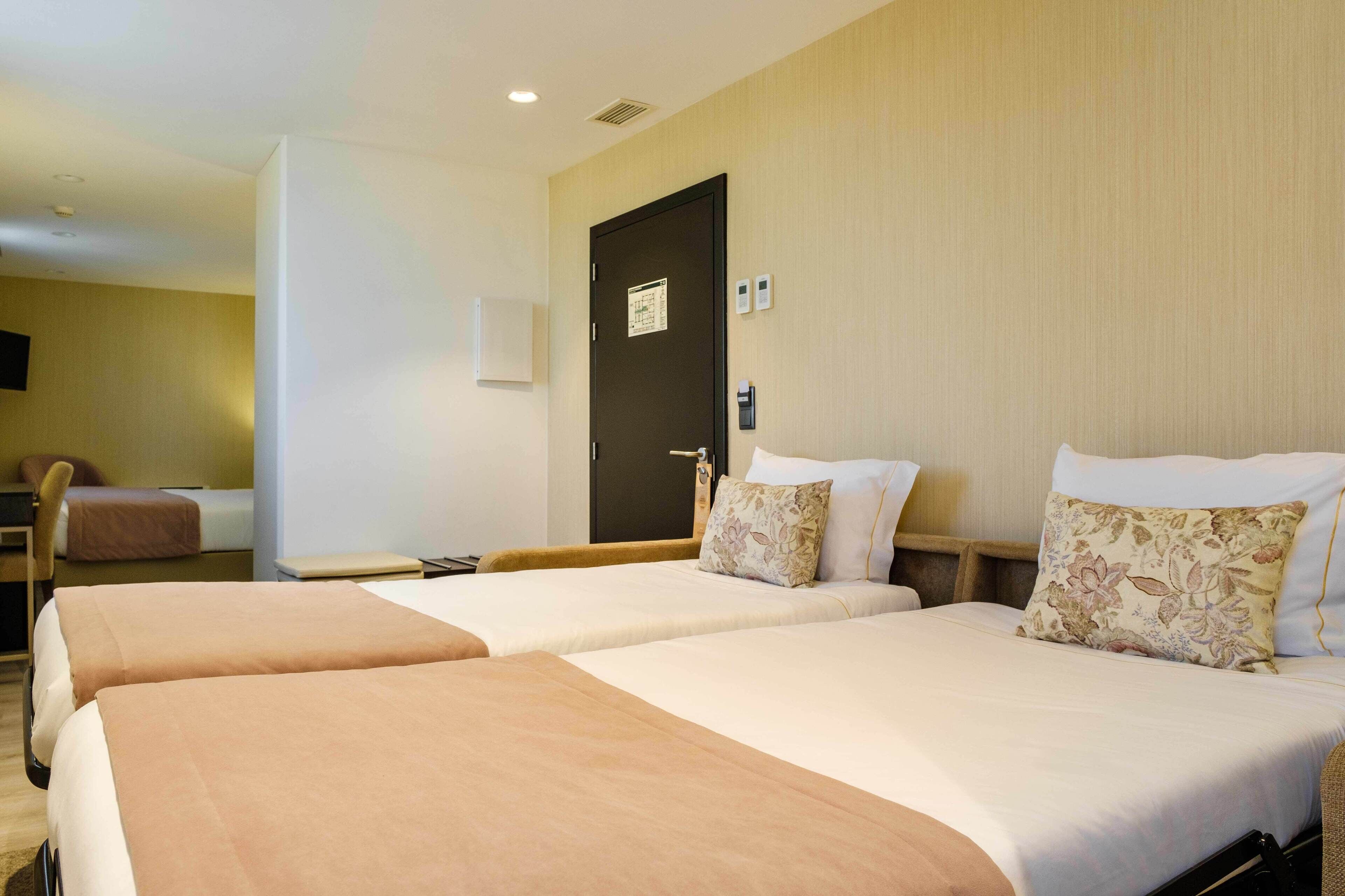 A hotel room with two beds, a desk, a chair, and a door with a map.
