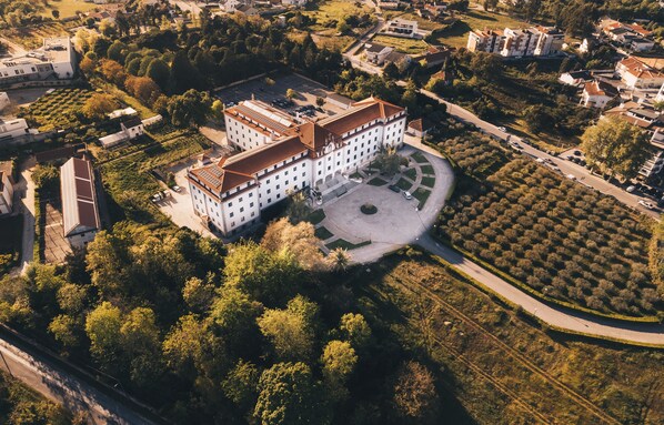 Une vue aérienne d’un grand bâtiment historique à la façade symétrique, entouré d’une végétation luxuriante et d’un jardin bien entretenu.