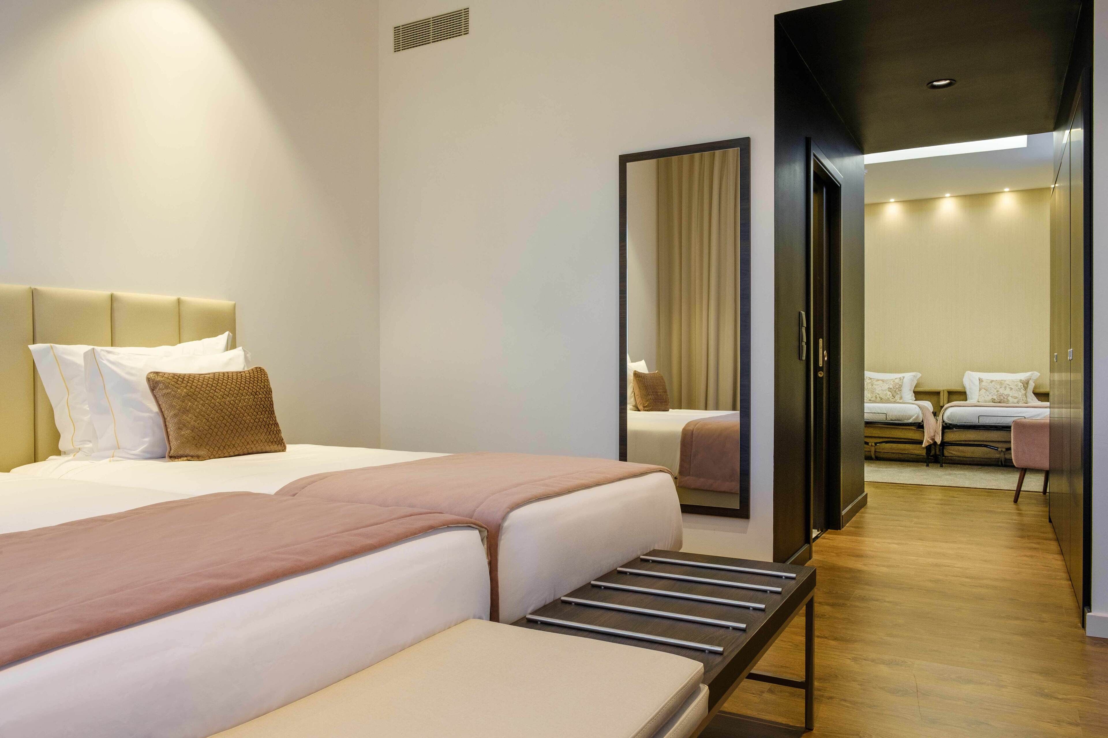 Ein Hotelzimmer mit einem großen Bett, Nachttischen, einem Spiegel und Blick in den angrenzenden Raum.