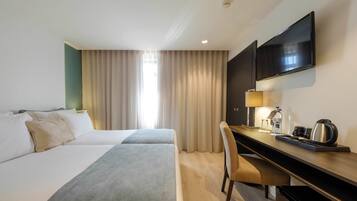 A hotel room with two beds, a desk, a chair, a TV, and a window with curtains.