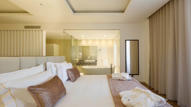 A modern hotel room with a large bed, a separate sitting area, a bathtub, and a large mirror. - SDivine Fátima Hotel (Ourem)