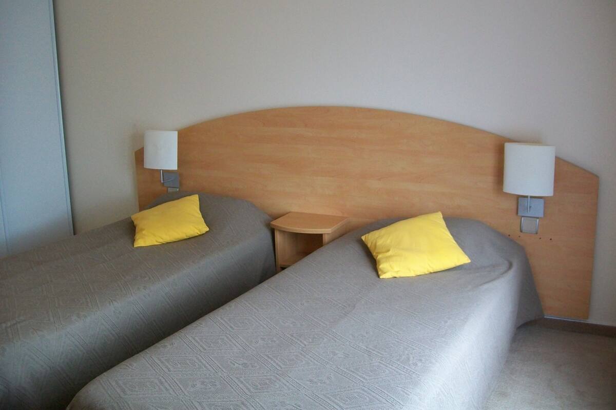 A hotel room with two single beds, each with a pillow and a bedside table.
