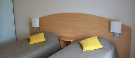 A hotel room with two single beds, each with a pillow and a bedside table.