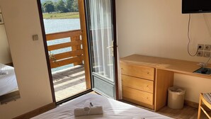 Een hotelkamer met een bed, een houten bureau, een televisie en een balkon met uitzicht op de zee en de bergen.