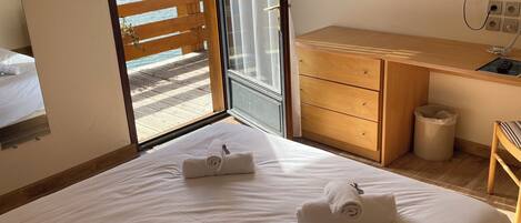 Habitación de hotel con cama, escritorio de madera, televisor y balcón con vistas al mar y las montañas.