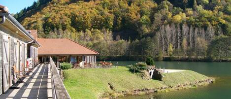 Un hotel junto al lago con una terraza con vistas a un lago tranquilo, rodeado de colinas boscosas.