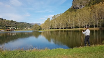 Un lago tranquilo con una persona tomando una fotografía, rodeado de árboles y un pueblo distante.