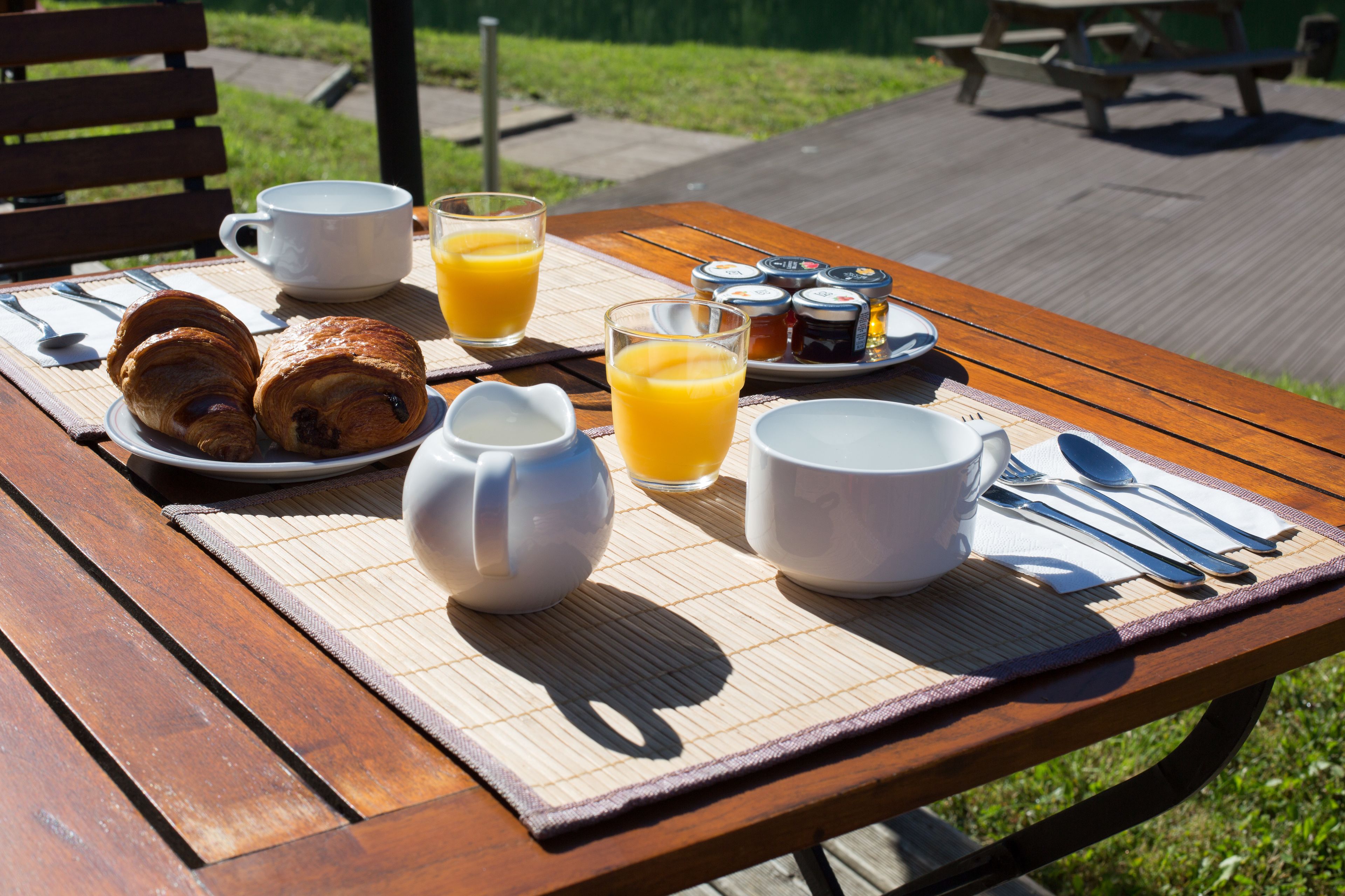 Una mesa de picnic de madera con productos para el desayuno, incluyendo cruasanes, jugo y condimentos.