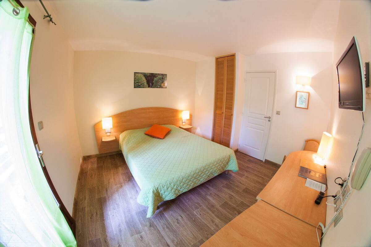 A bedroom with a bed, bedside lamps, a wooden dresser, a TV, and a door.