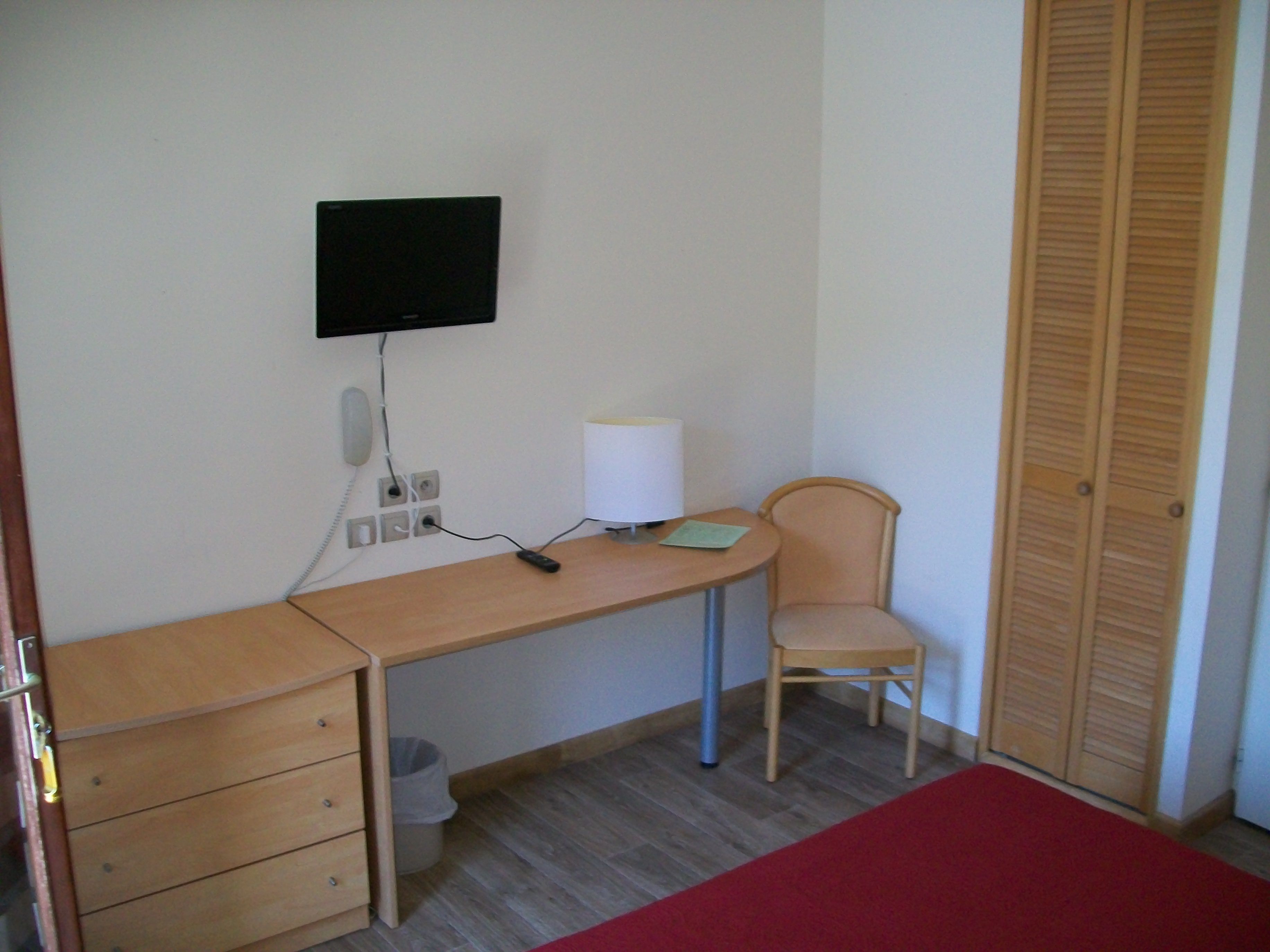 Ein Schlafzimmer mit Holztisch, Stuhl, Bett, Wandfernseher und Kleiderschrank.