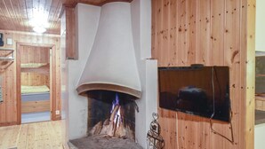 A cozy room with a fireplace, wooden walls, and a television mounted on the wall.