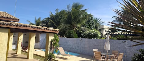 A pool area with a tiled wall, lounge chairs, and a small palm tree.