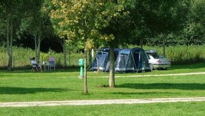 A campsite with tents, a car, and a person sitting on a chair. - Mobilhome Camping Arquebuse (Athée)