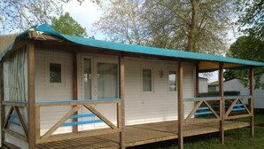 A wooden mobile home with a covered porch and a small deck. - Mobilhome Camping Arquebuse (Athée)