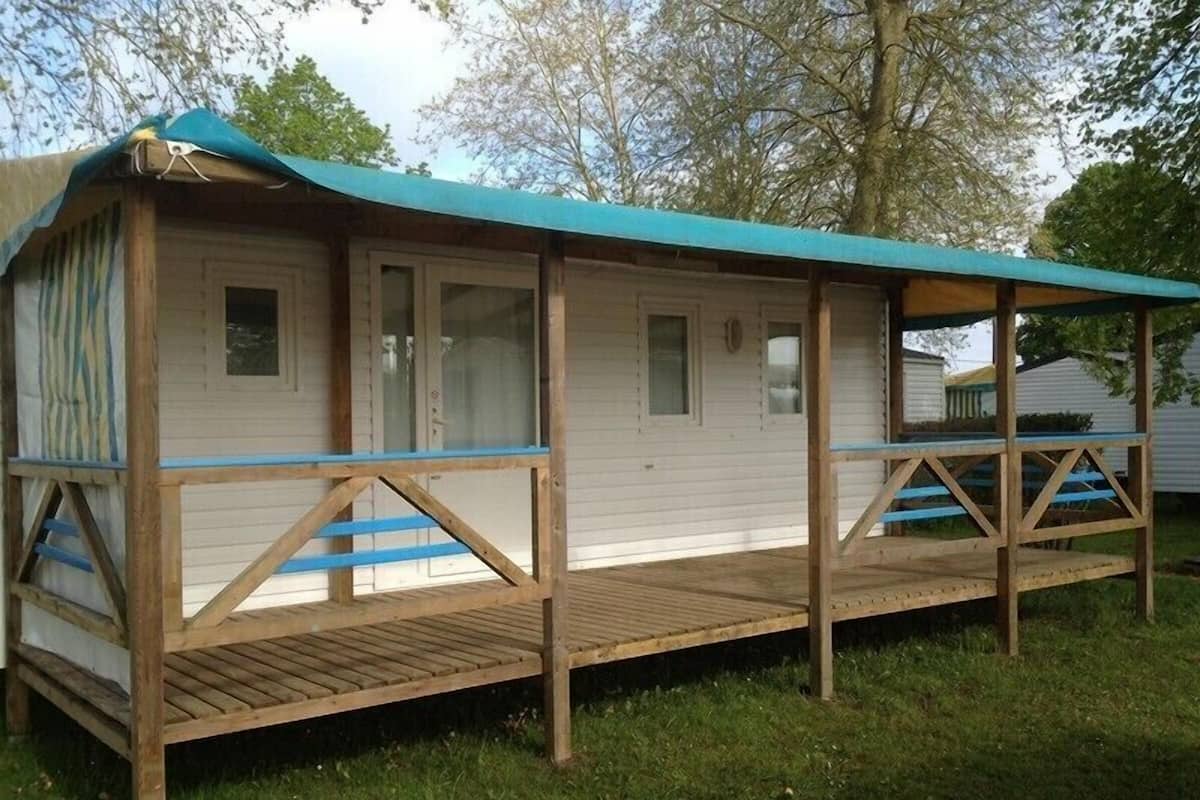 Ein Holz-Mobilheim mit überdachter Veranda und kleiner Terrasse.