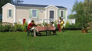 A mobile home with a checkered tablecloth, a dining table, and a person seated at the table. - Mobilhome Camping Arquebuse (Athée)