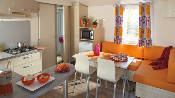 A compact kitchen with a gas stove, microwave, and a dining area with a table and chairs. - Mobilhome Camping Arquebuse (Athée)
