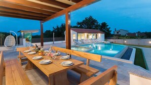 An outdoor dining area with a pool, wooden tables, and lounge chairs. - Lovely home in Marcana with sauna (Marcana)