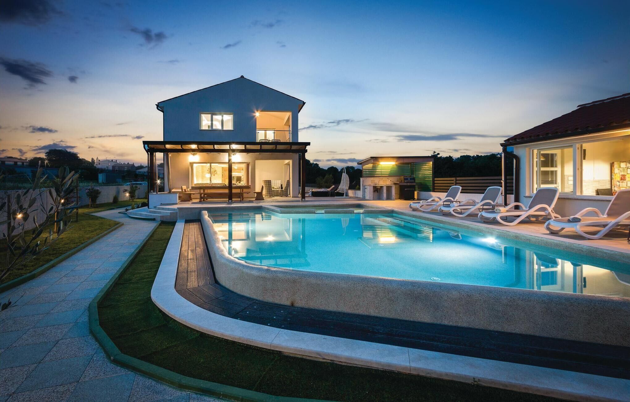 A modern house with a swimming pool, lounge chairs, and a covered patio area.