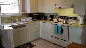 A compact kitchen with white cabinets, a microwave, a stove, and a sink. - Cottage by the Sea (Anacortes)