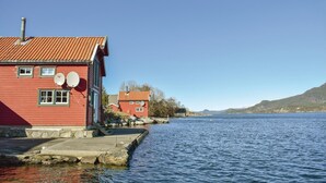A red building with satellite dishes, a dock extending into a calm lake, and a clear blue sky. - 2 bedroom gorgeous home in ølensvåg (Ølensvåg)