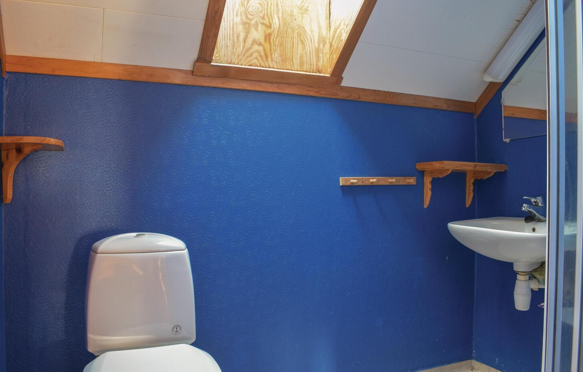 A bathroom with a blue wall, a white toilet, a white sink, and wooden shelves.
