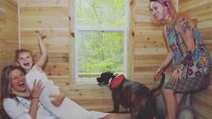 Interior de una cabaña de madera con una ventana, un perro y dos personas.