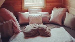 Una habitación de cabaña acogedora con un ventanal grande, paredes de madera y una cama con muchas almohadas.