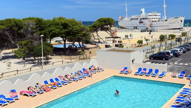 A swimming pool with lounge chairs, a large ship in the background, and a clear sky.