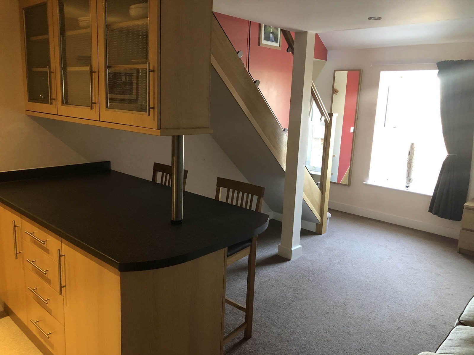A kitchen with a dark countertop, wooden cabinets, and a chair. There is a staircase leading to another room.