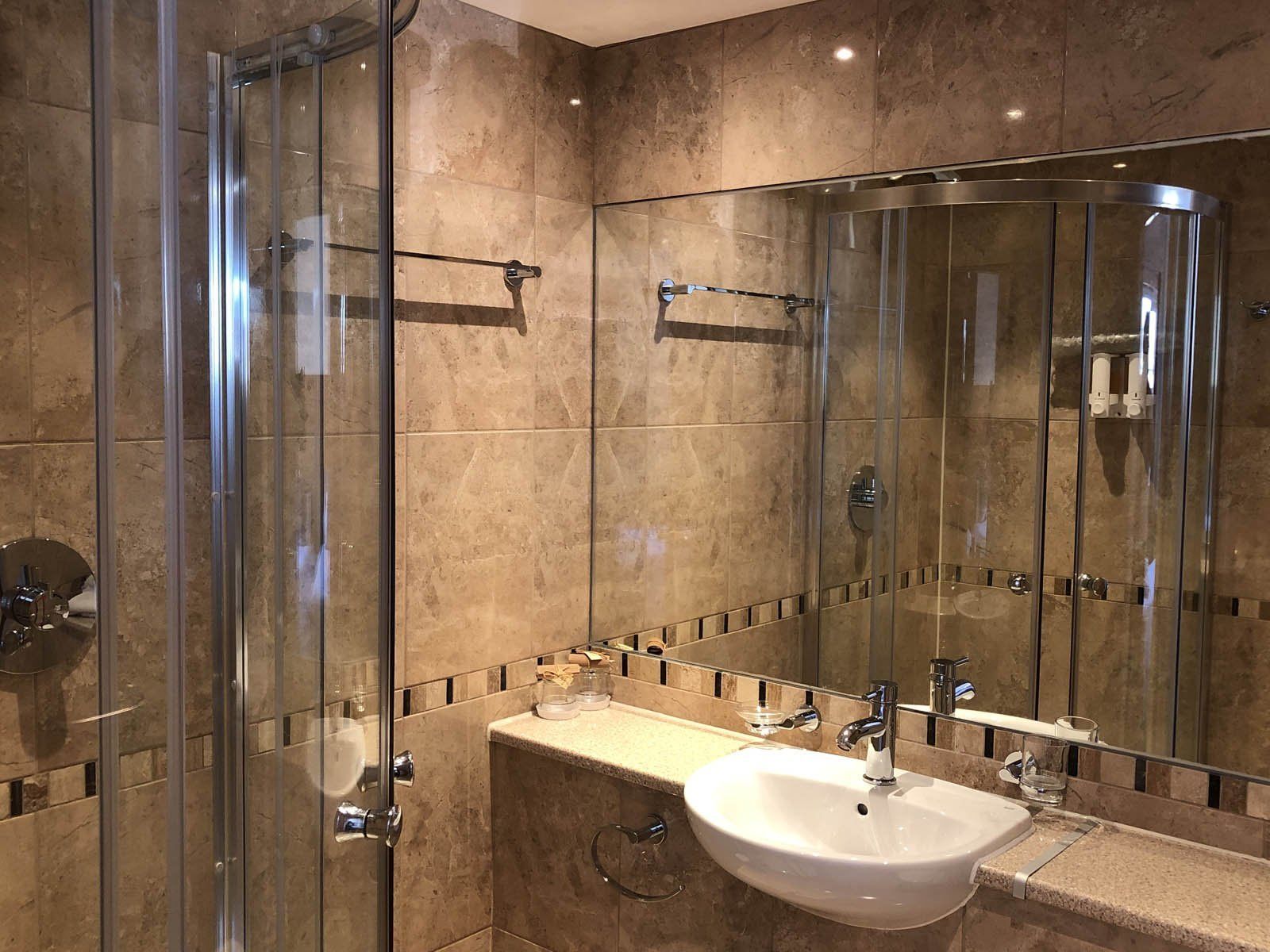 Een moderne badkamer met een douchecabine van glas, een grote spiegel en een witte wastafel.