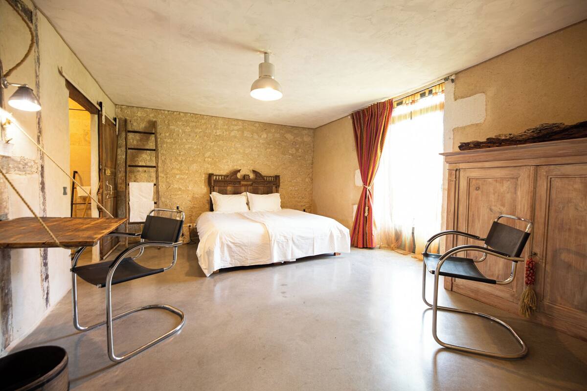 Ein Schlafzimmer mit einem Bett, zwei Stühlen mit Metallgestell, einem Holzschrank und einer Steinwand.