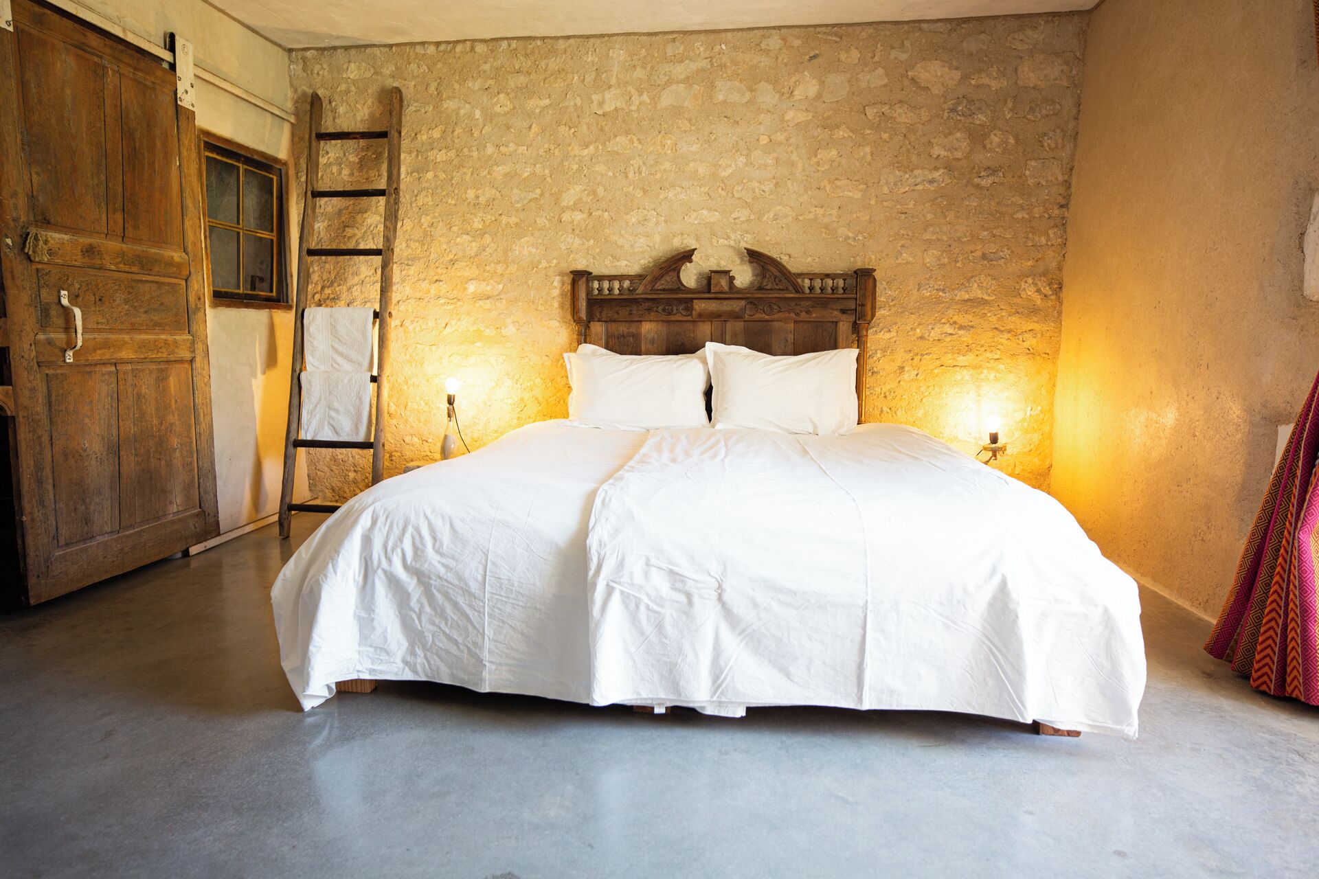 A large bed with a wooden headboard in a room with stone walls and a wooden door.
