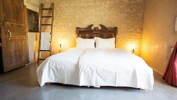 A large bed with a wooden headboard in a room with stone walls and a wooden door.